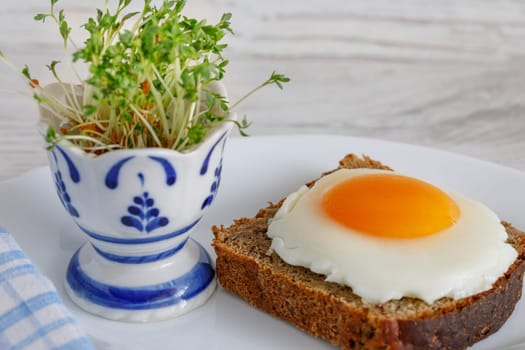 Fried eggs on a piece of whole-grain rustic bread with a salad dressing in an egg stand