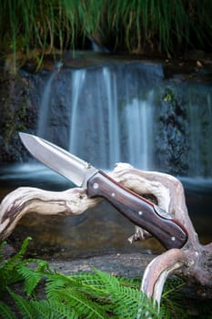 knife for bushcraft and survival in the wild near to a waterfall