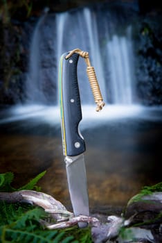 knife for bushcraft and survival in the wild near to a waterfall