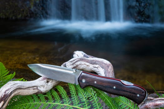 knife for bushcraft and survival in the wild near to a waterfall