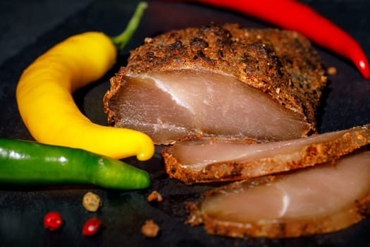 Dried chicken breast in spices, with colorful chili peppers around, against a dark background