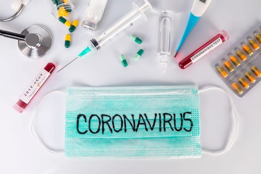 Protective medical mask with Coronavirus text and medical ampoules stethoscope thermometer and pills. Virus test and research for treatment concept.