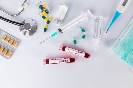 Blood test tube with the Coronavirus disease for virus test and research. Blood test tube with protective masks, medicines, thermometer, stethoscope and syringe on a white background.
