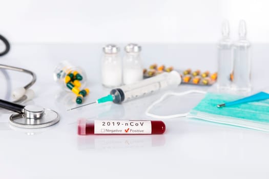 Blood test tube with the Coronavirus disease for virus test and research. Blood test tube with protective masks, medicines, thermometer, stethoscope and syringe on a white background.
