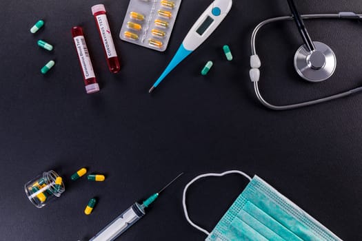 Blood test tube with the Coronavirus disease for virus test and research. Blood test tube with protective masks, medicines, thermometer, stethoscope and syringe on a black background.