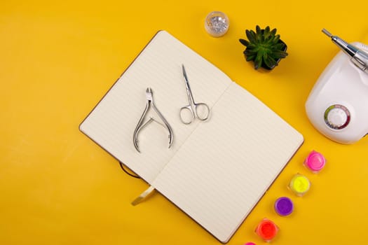 Set of cosmetic tools for manicure and pedicure on an orange background. Nearby there is an open notebook for writing, gel varnishes, a mill, nail files, scissors and nippers. Top views with clear space