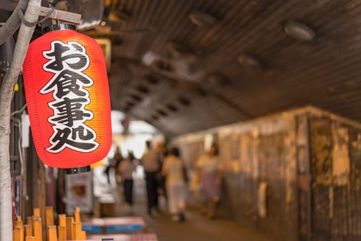 Traditional retro red rice paper lantern where it is written "Oshokujidokoro"" which means ""Meal"" on underpass Yurakucho Concourse wall under the railway line of the station Yurakucho. Japanese noodle stalls and sake bars revive the nostalgic years of Showa air with old posters and placards glued to the walls of the tunnel."