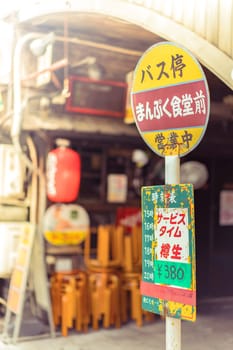 Restaurant sign immitating an old retro bus stop sign on underpass Yurakucho Concourse wall under the railway line of the station Yurakucho. Japanese noodle stalls and sake bars revive the nostalgic years of Showa air with old posters and placards glued to the walls of the tunnel.