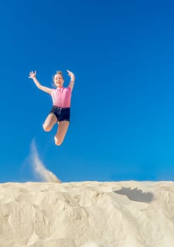 a young girl jumps in the summer from a yellow sand dune