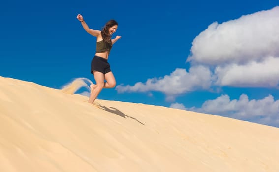 a girl runs from a sand dune full of zest for life in the summer, whirling up dust