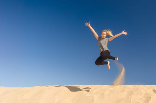 a young girl jumps in the summer from a yellow sand dune