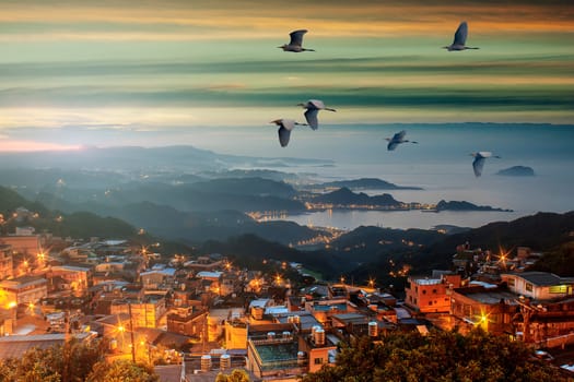 The Foggy morning in the mountains with flying birds over silhouettes of hills