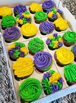 Two dozen colorful, purple, lime green and golden yellow Mardi Gras, chocolate, cupcakes in a bakery box.