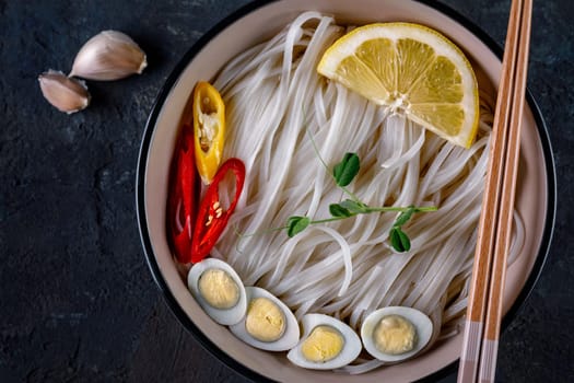 Rice noodles Asian cuisine with quail eggs, chili pepper and lemon, and green pea sprout
