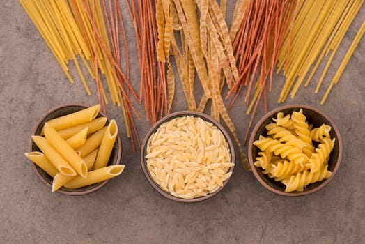 Mix of pasta made from wheat semolina, quinoa and azuki beans on a brown textured background, ingredients italian food