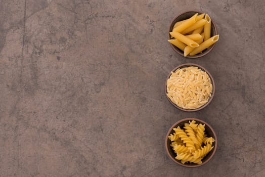 Mix of pasta made from wheat semolina, quinoa and azuki beans on a brown textured background, ingredients italian food