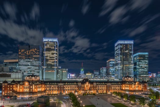 Night panoramic view of Marunouchi side of Tokyo railway station in the Chiyoda City, Tokyo, Japan.  The station is divided into Marunouchi and Yaesu sides in its directional signage. The station first called Central Station was built in 1914 directly in front of the Imperial Palace gardens. The three-story station building was designed by architect Tatsuno Kingo who also designed Manseibashi Station and the nearby Bank of Japan building. Much of the station was destroyed in B-29 firebombing on May 25, 1945. The bombing shattered the impressive rooftop domes. The station was quickly rebuilt within the year, but simple angular roofs were built in place of the domes, and the restored building was only two stories tall instead of three.