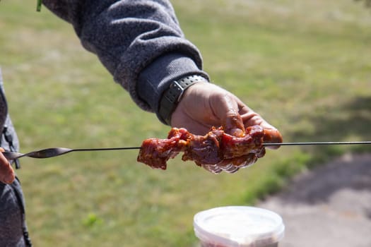 Hands of a man putting meat on skewer for barbecue. Close-up image of uncooked meat on skewer.