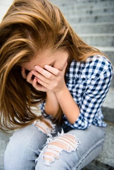 Unhappy depressed teenager with face in hands sitting outdoor