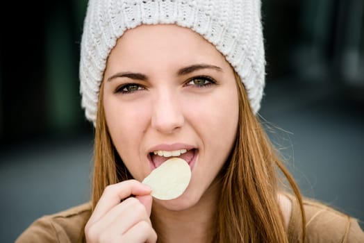 Teenager girl in cap eating chips outdoor in street