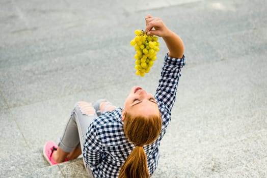 Young woman eating grapes outdoor sitting on stairs - above view