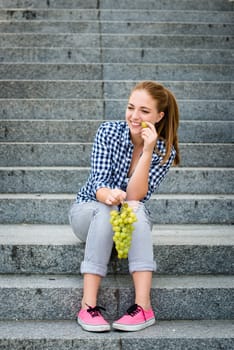 Young woman - teenage girl eating grapes outdoor sitting on stairs