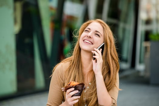 Teenager eating muffin in street and browsing internet on phone