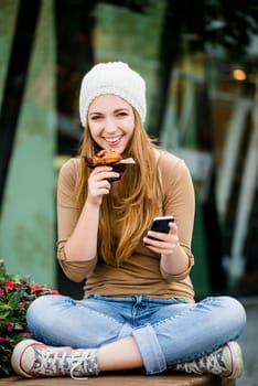 Teenager - young woman eating muffin in street and looking in phone