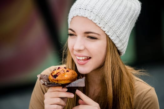 Young woman - teenager in cap eating muffin outdoor in street