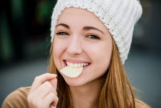Teenager girl in cap eating chips outdoor in street