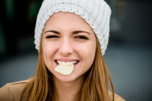 Teenager girl in cap eating chips outdoor in street