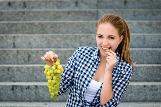 Young woman - teenage girl eating grapes outdoor sitting on stairs