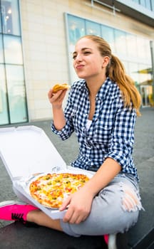 Teenager lifestyle - young woman eating pizza outdoor in street