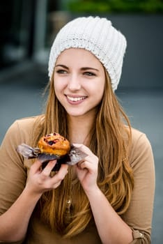 Young woman - teenager in cap eating muffin outdoor in street