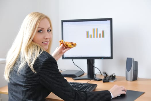 Young smiling business person working with computer eating pizza