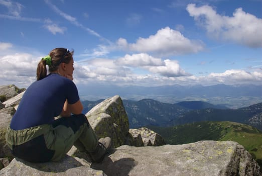 Hiking woman siting on rocks looks at beautiful  mountains and blue sky