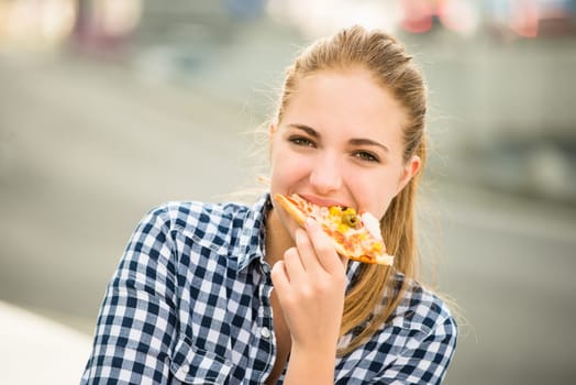 Teenager lifestyle - young woman eating pizza outdoor in street