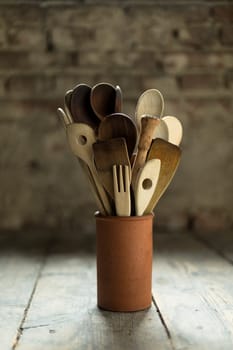 old wooden spoons in a clay vase on a deal board floor in front of a brick wall
