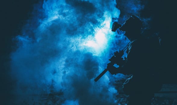 Silhouette of modern infantry soldier, elite army fighter in tactical ammunition and helmet, standing with assault service rifle in hands in the smoke