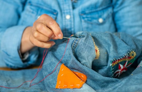 an elderly woman hands sewing on fabric jeans, needle.