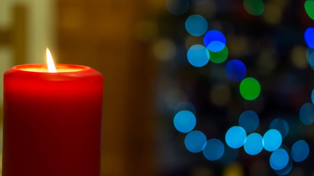 One large red burning candle on abstract blurred background with big circular colourful bokeh