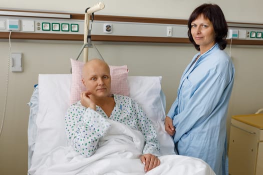Woman without hair after chemotherapy patient lying at hospital bed feeling sad and depressed worried. A friend came to please her. Health care and clinical attention concept.