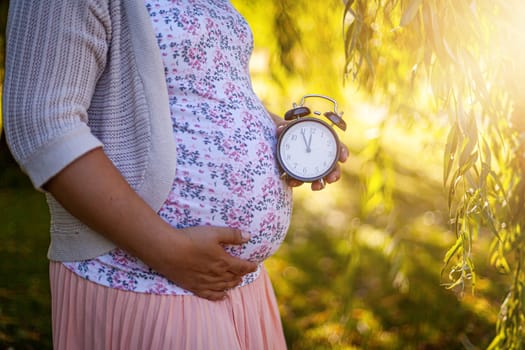 A pregnant women in a white dress in park holding a clock. High quality photo