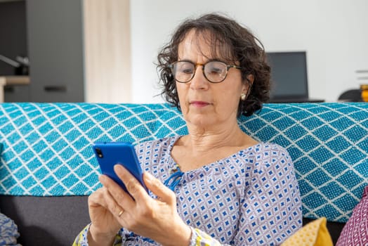 a cheerful brunette senior woman using smartphone while sitting on sofa