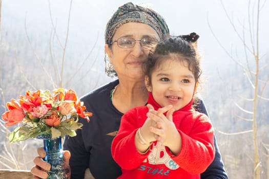 Close up portrait of a happy little with her senior Muslim grandmother having a flower vase in right hand, togetherness concept