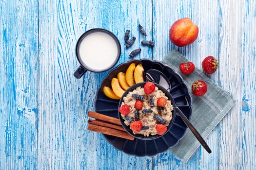 Mug with yogurt and oatmeal porridge with fresh berries and fruit in dark blue bowl on blue wooden background. Top view with copy space. Concept of healthy lifestyle, healthy food, dieting