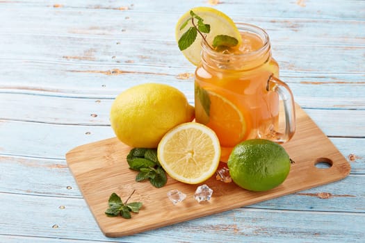 Citrus lemonade with ice, leaves of mint, lemon and lime slices standing on blue wooden table. Homemade lemonade with citruses. Healthy cool beverage