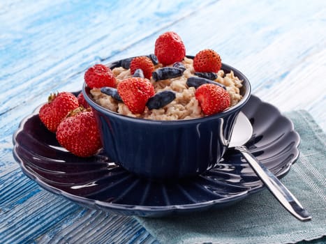 Oatmeal porridge with fresh berries in dark blue bowl on blue wooden background. Concept of healthy lifestyle, healthy food, dieting, vegetarian food
