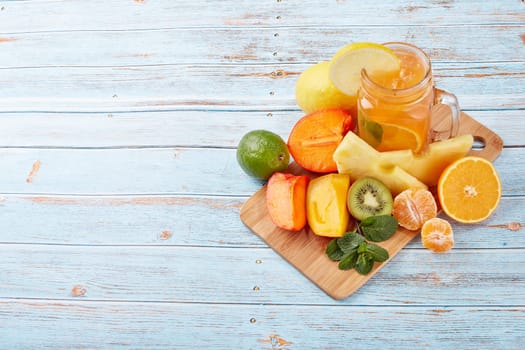 Fruit lemonade with ice, leaves of mint, lemon, pineapple, mango and lime slices standing on blue wooden table. Homemade lemonade with mix fruits. Healthy cool beverage, fruit juice. Top view