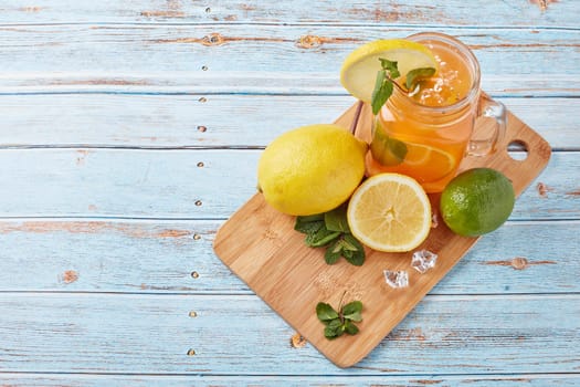 Citrus lemonade with ice, leaves of mint, lemon and lime slices standing on blue wooden table. Homemade lemonade with citruses. Healthy cool beverage